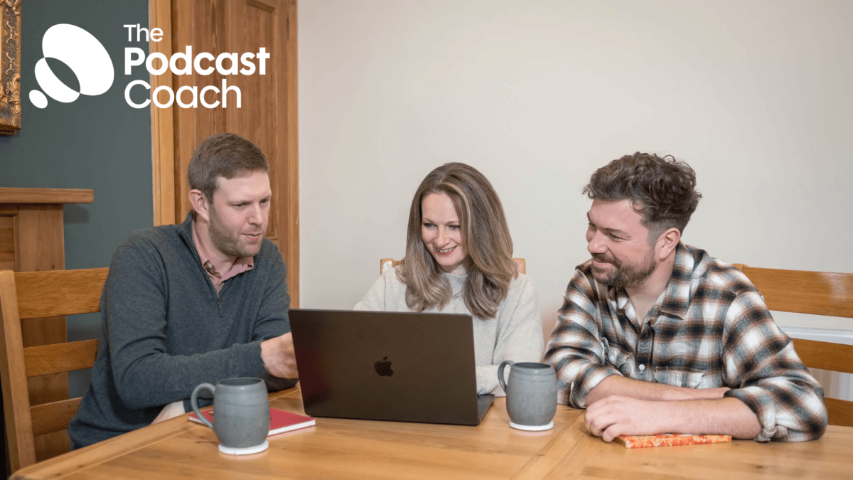 Rory, Lizi and Ben - the podcast coach team - sit around a table with mugs and notebooks discussing podcast marketing strategy.